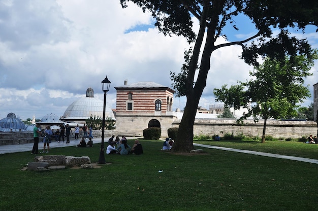 People are resting on a green lawn. Summer panorama. Old buildings made of stone on a background of the sky with clouds. 09 July 2021, Istanbul, Turkey.