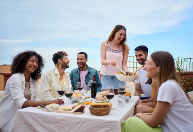 人々は食べ物とワインを共有しテーブルの周りで笑顔で暇な時間を楽しんでいます