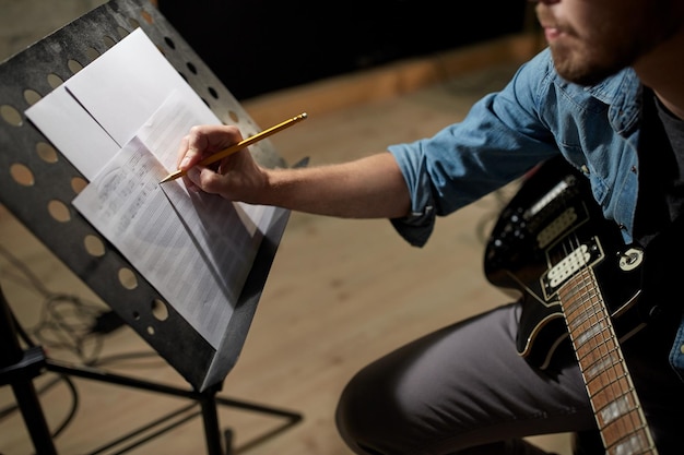 Concetto di persone, arte e intrattenimento - uomo con la chitarra che scrive note al libro di musica in studio