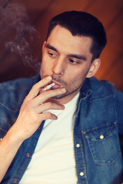 people and bad habits concept - young man smoking cigarette at bar