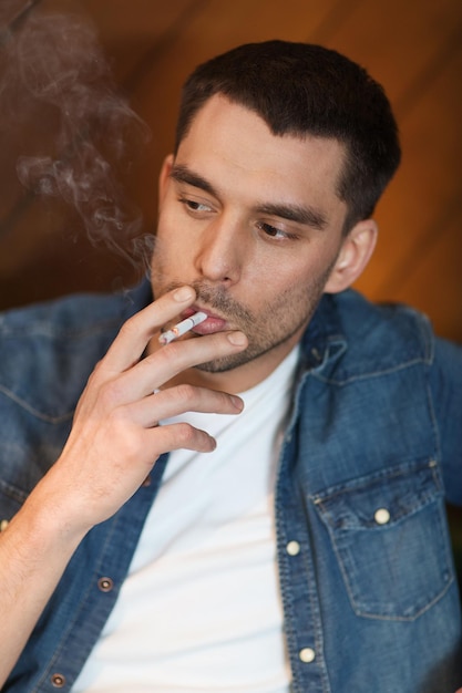 Foto concetto di persone e cattive abitudini - giovane uomo che fuma sigaretta al bar
