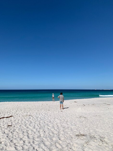 People on beach against clear blue sky