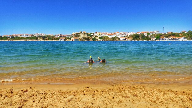 People on beach against clear blue sky