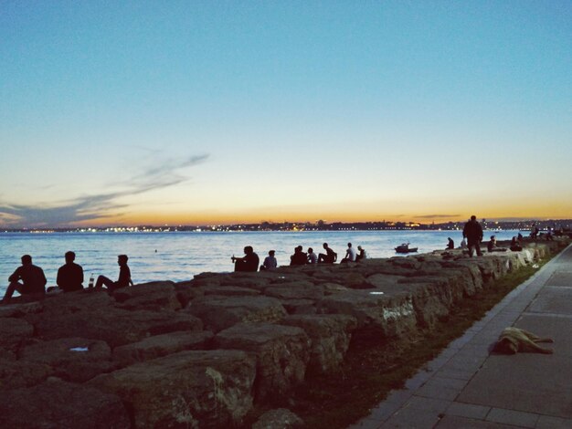 People at beach against sky during sunset