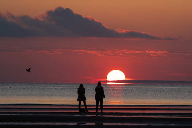 People on beach enjoy beautiful sunset in autumn season look at sun setting in sea and colorful sky