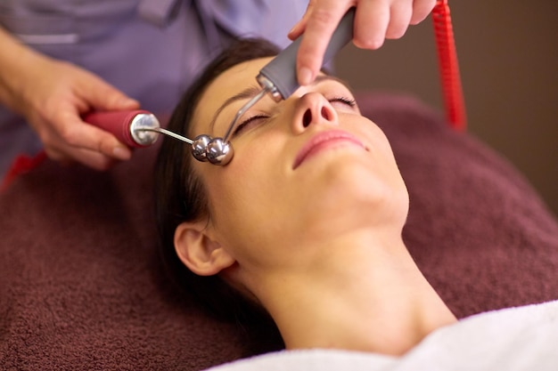 people, beauty, cosmetology and technology concept - beautiful young woman having needle free mesotherapy or hydradermie facial treatment by microcurrent firming device in spa