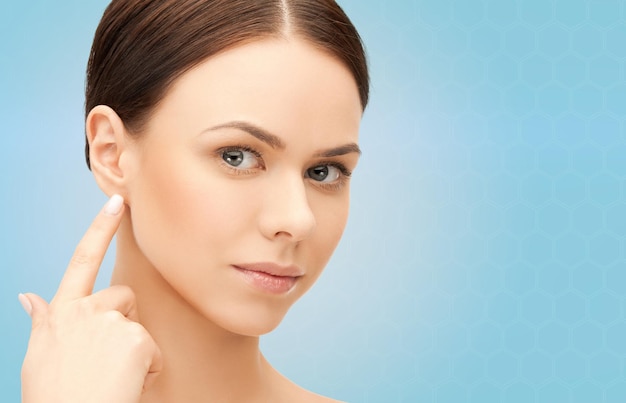 people, beauty, hearing and healthcare concept - face of beautiful woman touching her ear over blue background