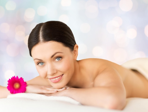 people, beauty, holidays and body care concept - happy beautiful woman lying on massage desk at spa over blue lights background