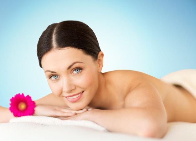 people, beauty, spa and body care concept - happy beautiful woman lying on massage desk at spa over blue background