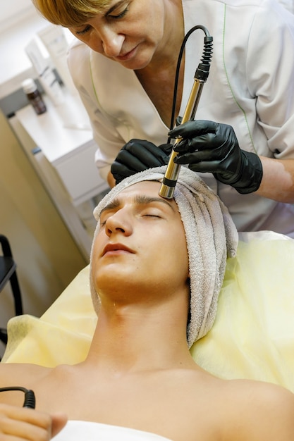 People, beauty, spa, cosmetology and technology concept - Cosmetologist makes the procedure microcurrent therapy of the facial skin of a beautiful, young man in a beauty salon