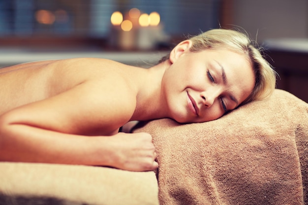 people, beauty, spa, healthy lifestyle and relaxation concept - beautiful young woman lying on massage table in spa