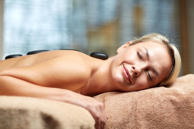 люди, красота, спа, здоровый образ жизни и концепция релаксации - крупный план красивой молодой женщины, делающей массаж горячими камнями в спа