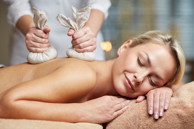 people, beauty, spa, healthy lifestyle and relaxation concept - close up of beautiful young woman lying and having herbal bag massage in spa