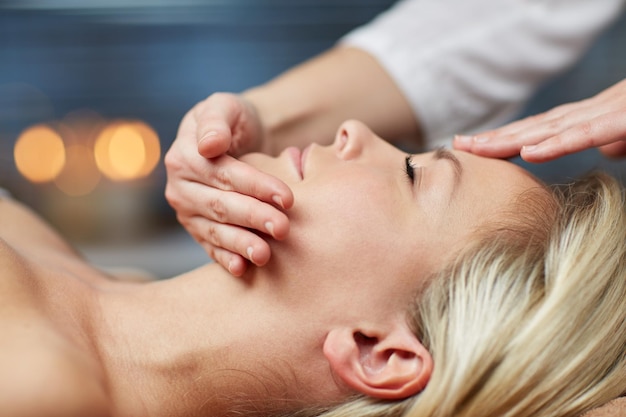 people, beauty, spa, healthy lifestyle and relaxation concept - close up of beautiful young woman lying with closed eyes and having face or head massage in spa