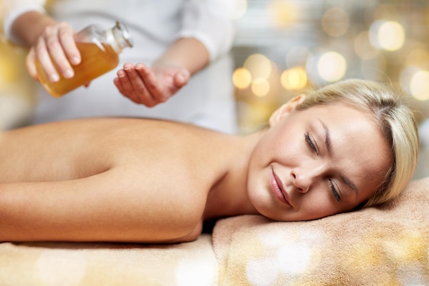 Foto persone, bellezza, spa, stile di vita sano e concetto di relax - primo piano di bella giovane donna sdraiata con gli occhi chiusi sul lettino da massaggio e terapista che tiene una bottiglia di olio nella spa