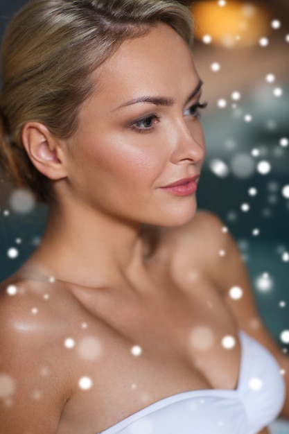 people, beauty, spa, healthy lifestyle and relaxation concept - close up of beautiful young woman in swimsuit at swimming pool with snow effect