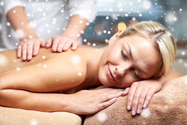 people, beauty, spa, winter and relaxation concept - close up of beautiful young woman lying with closed eyes and having hand back massage in spa salon with snow effect