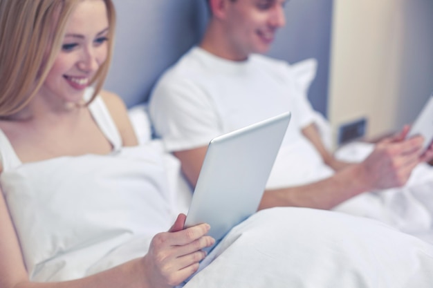 people, bedtime, technology and relations concept - close up of smiling couple in bed with tablet pc computers