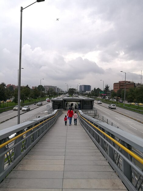 People on bridge in city against sky