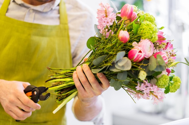 people, business, sale and floristry concept - close up of florist man making bunch and cropping stems by pruner at flower shop