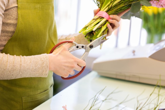 人、ビジネス、販売、フローリストリーのコンセプト – 花屋で束を作り、はさみで茎を切り取る花屋の女性の接写