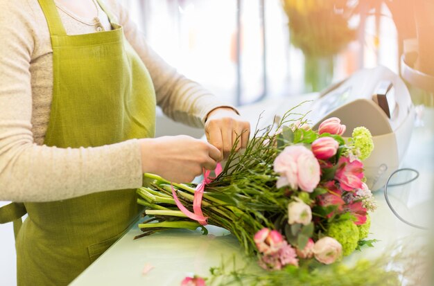 people, business, sale and floristry concept - close up of florist woman making bunch at flower shop