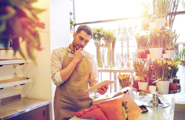 Photo people, business, technology, sale and floristry and concept - florist man with tablet pc computer thinking at flower shop counter