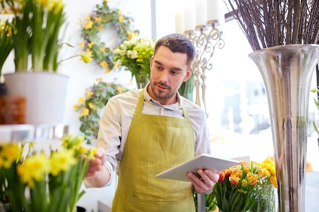 people, business, technology, sale and floristry and concept - happy smiling florist man with tablet pc computer at flower shop