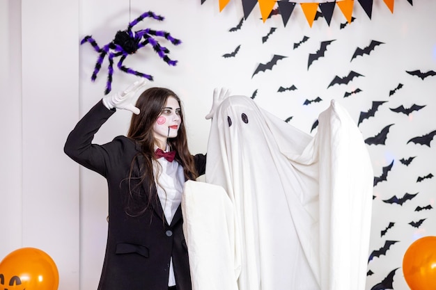 People in carnival costumes of a ghost and a scary doll on a Halloween holiday on a decorated background with bats and spiders and balls