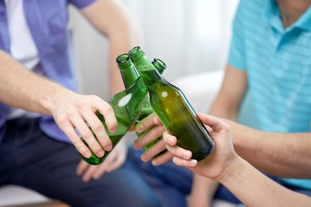 люди, праздник и концепция алкоголя - крупный план друзей, звенящих пивными бутылками дома