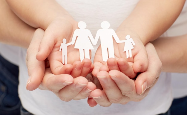 people, charity, family and care concept - close up of woman and girl hands holding paper family cutout