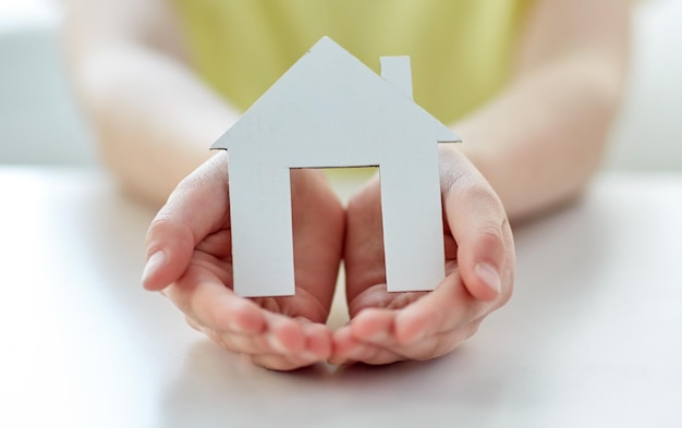 Foto concetto di persone, carità, famiglia e casa - primo piano di una ragazza felice che tiene un ritaglio di casa di carta nelle mani a coppa