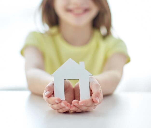 people, charity, family and home concept - close up of happy girl holding paper house cutout in cupped hands