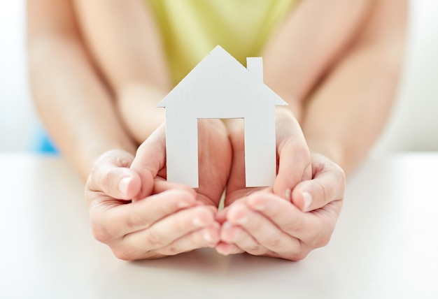 people, charity, family and home concept - close up of woman and girl holding paper house cutout in cupped hands