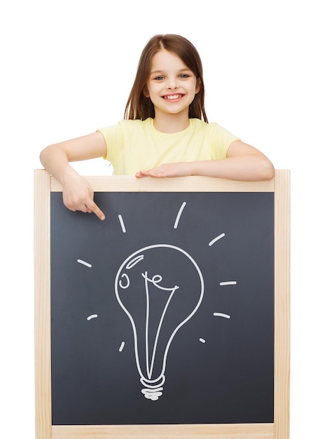 people, childhood and education concept - smiling little girl pointing finger to blackboard