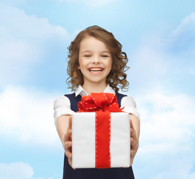 people, childhood, summer and holidays concept - happy smiling girl with gift box over blue sky background