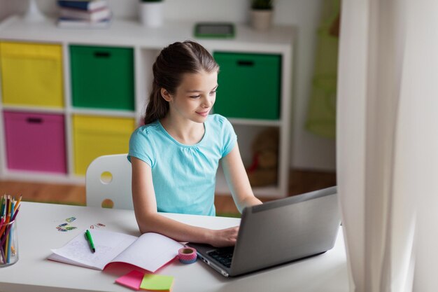 people, children, education and learning concept - happy girl typing on laptop at home