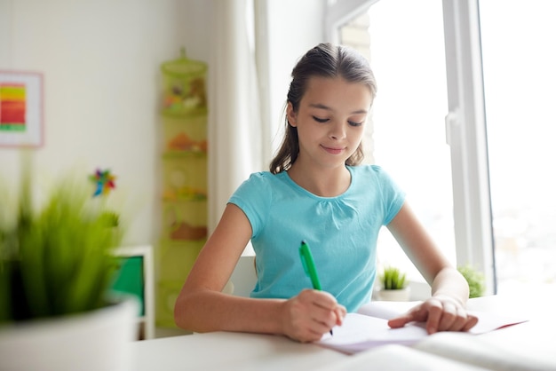 Photo people, children, education and learning concept - happy girl writing to notebook at home