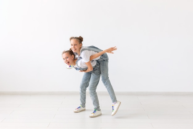 People, children and family concept - little girl carrying her twin sister piggyback on white background.