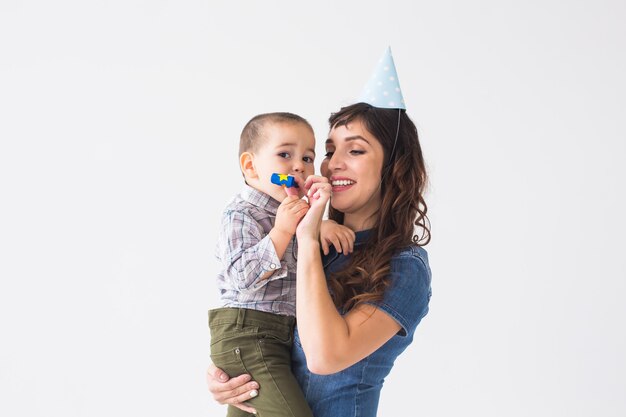 People, children and holiday concept - Charming mother hold her son wearing birthday cap over white wall with copy space.