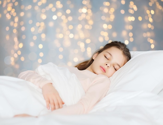 People children rest and comfort concept girl sleeping in bed over holidays lights background