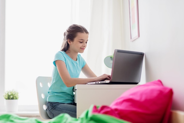 people, children and technology concept - girl typing on laptop computer at home