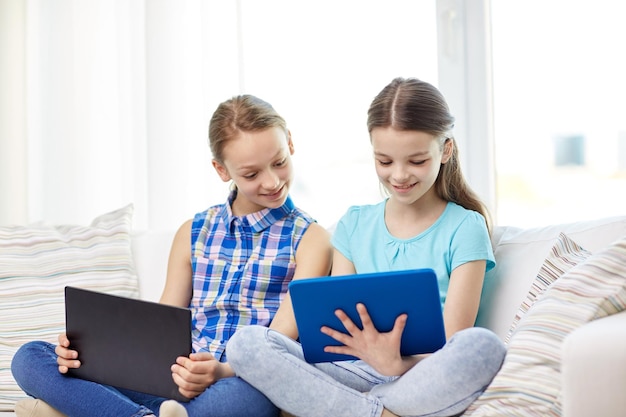 人、子供、テクノロジー、友達、友情のコンセプト – 家のソファに座るタブレットPCを持つ幸せな女の子