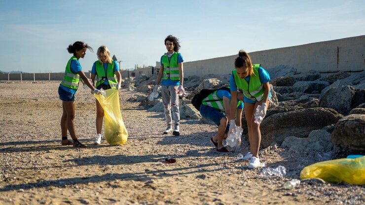 People cleaning up the beach volunteers collecting the waste on the coast line young students working in team aware of the pollution produced by the plastic industry