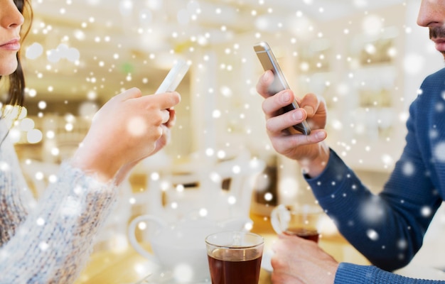 people, communication and technology concept - close up of couple with smartphones drinking tea at cafe or restaurant