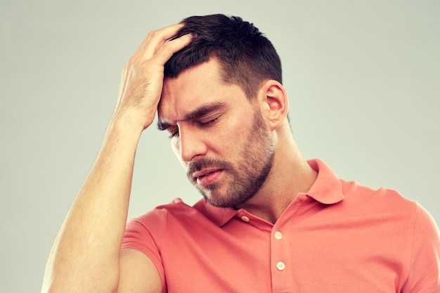 人、危機、感情、ストレスのコンセプト – グレイの背景に頭痛に苦しむ不幸な男性