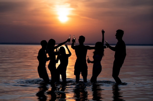 Le persone che ballano alla festa serale in spiaggia contro il tramonto