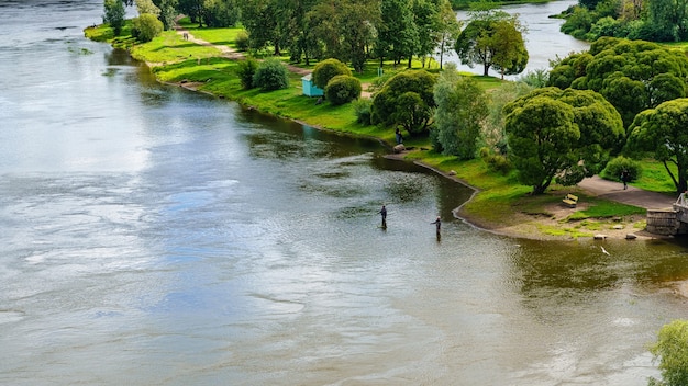 People in the distance fishing in a beautiful river full of vegetation on the shore.