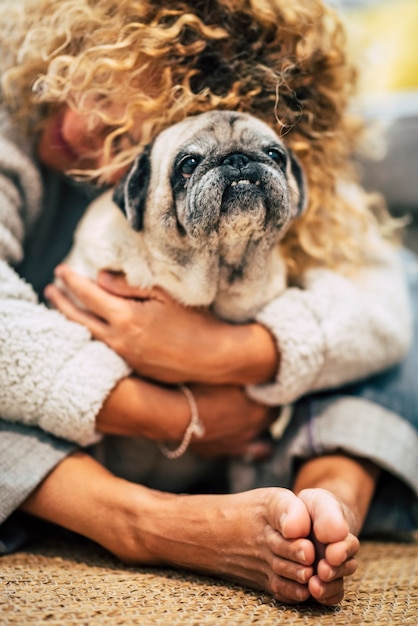 人々の犬の飼い主と親友はコンセプトが大好きです-女性は床に座って家で彼女のパグを抱きしめます-子犬の保護と友情療法