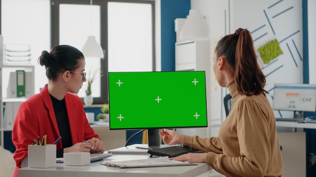 People doing teamwork with green screen on monitor. Women coworkers using computer display with isolated mock up template and chroma key copy space on blank background in office.